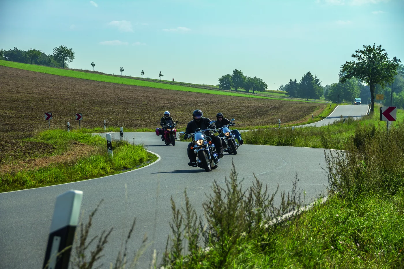 Mehrere Motorräder auf einer geschwungenen Landstraße durch Felder